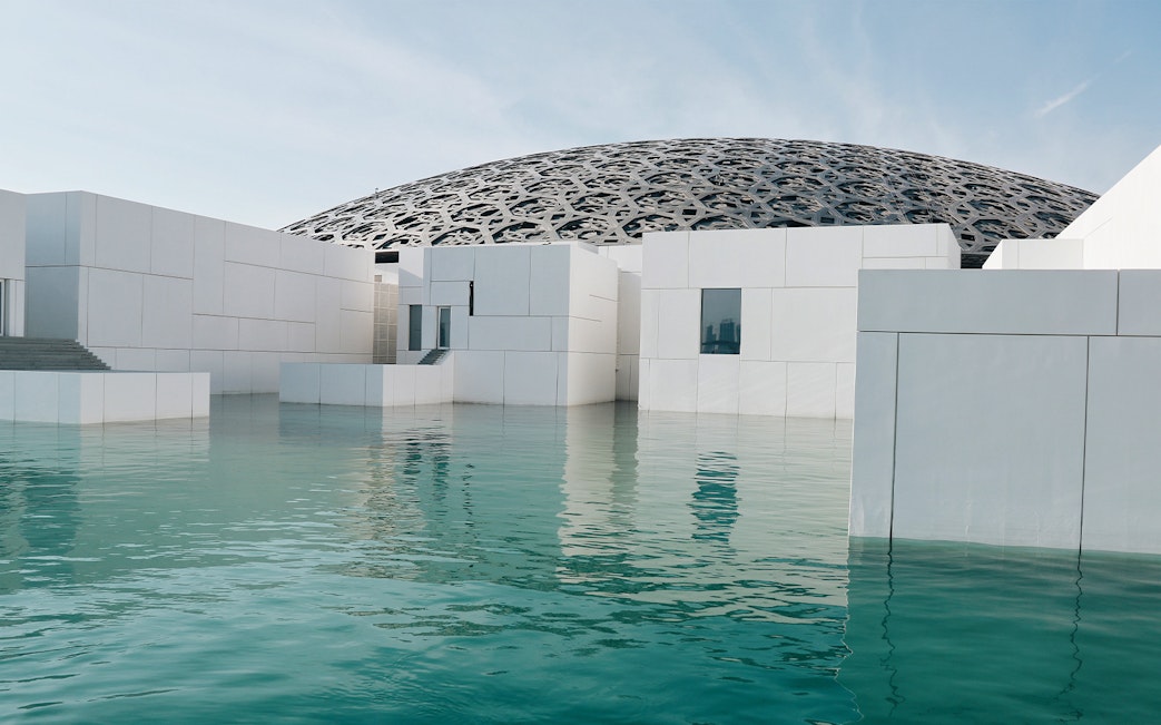 Louvre Abu Dhabi's dome and modern architecture reflected in water.