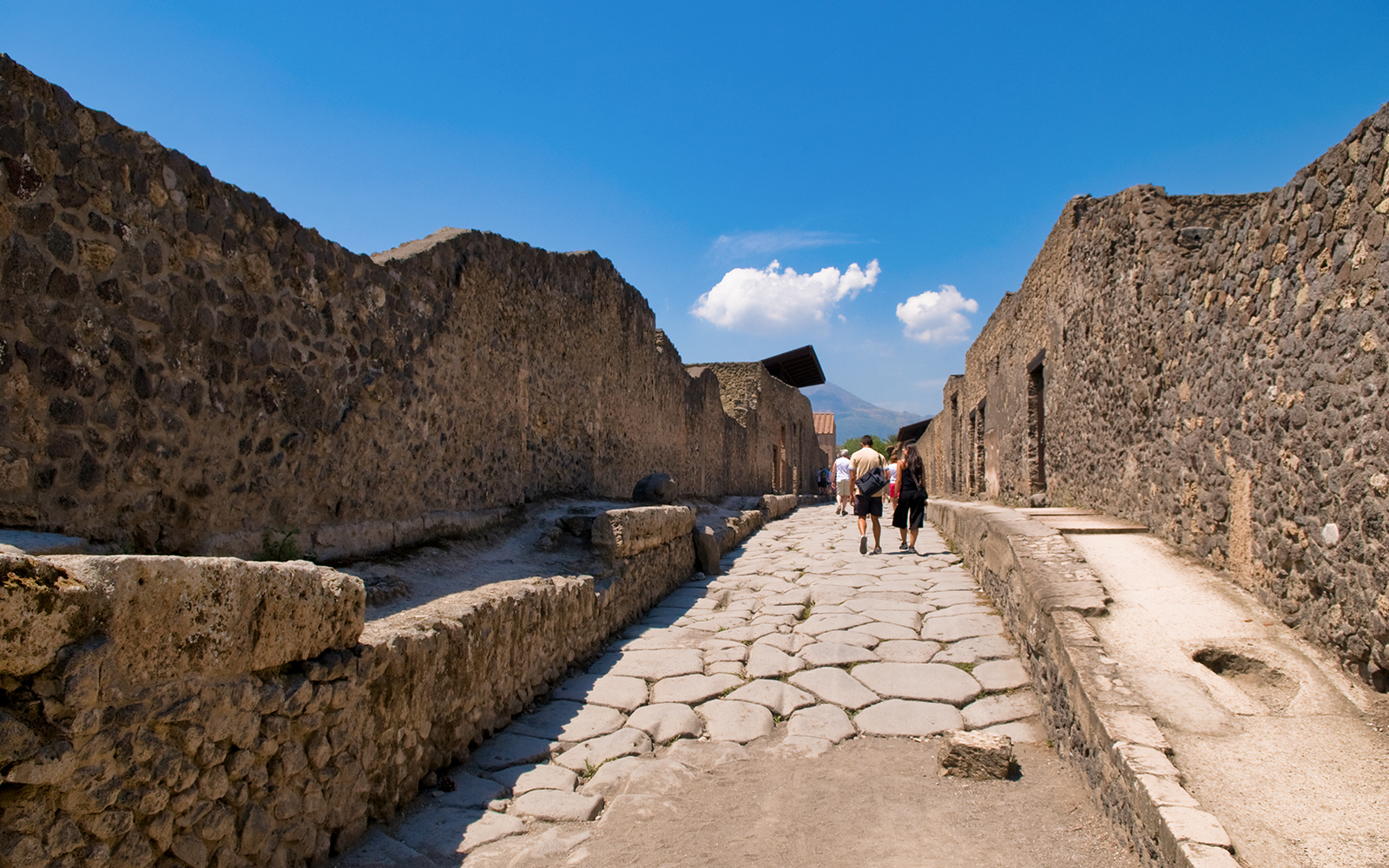 Visitors walking through ancient stone streets of Pompeii, Italy.