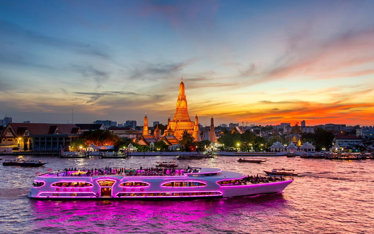 Cruise ship on Chao Phraya River at sunset near Wat Arun, Bangkok.