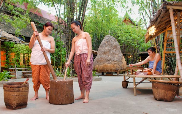 Women in traditional attire preparing food at Siam Niramit Bangkok cultural village.