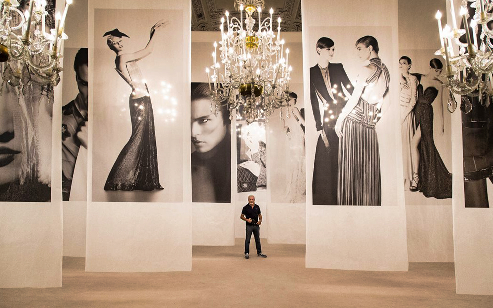 Fashion exhibit with large black-and-white portraits and chandeliers at Pitti Palace, Florence.