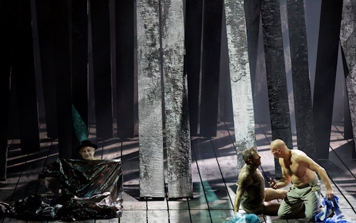 Actors performing a dramatic scene in a forest setting on stage.
