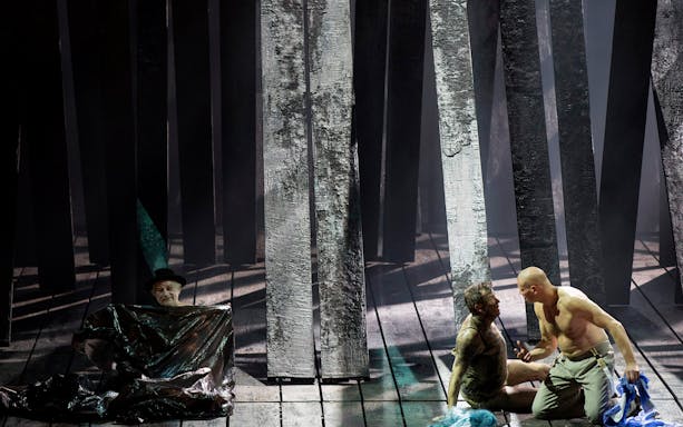 Actors performing a dramatic scene in a forest setting on stage.