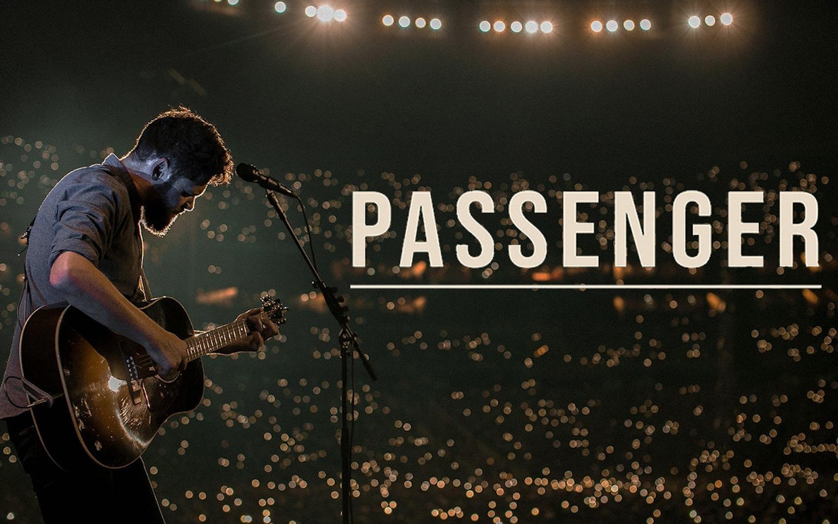 Musician performing live on stage with guitar, "Passenger" text in background.