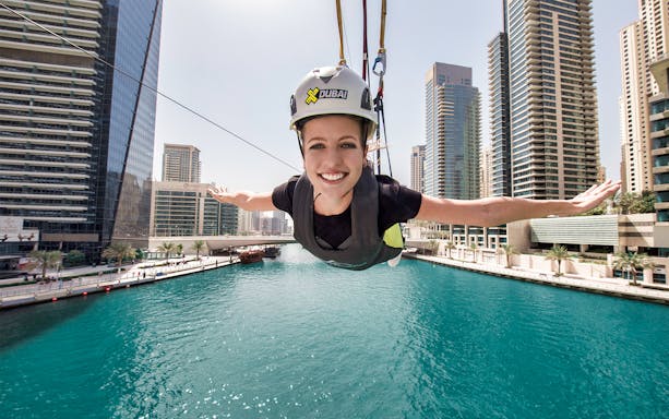 Person ziplining over Dubai Marina with skyscrapers in the background.