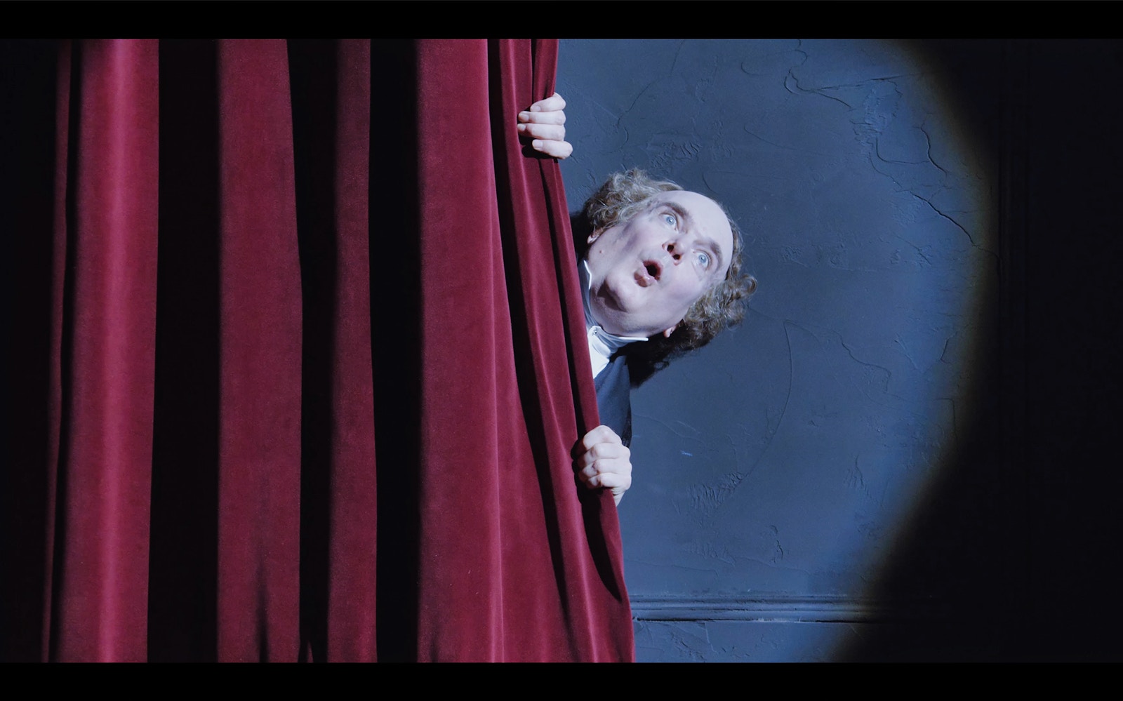 Man peeking from behind red theater curtain during "A Christmas Carol" performance.