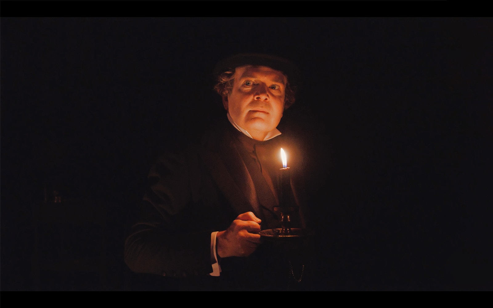 Man holding a candle in a dark scene from A Christmas Carol.