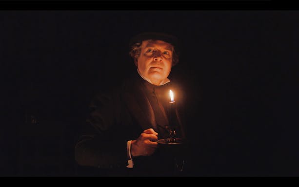 Man holding a candle in a dark scene from A Christmas Carol.