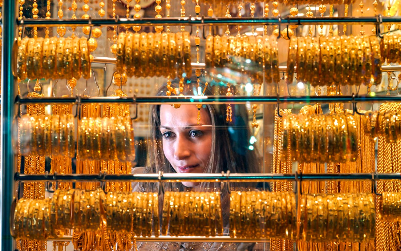 Woman admiring gold jewelry in Dubai market display.