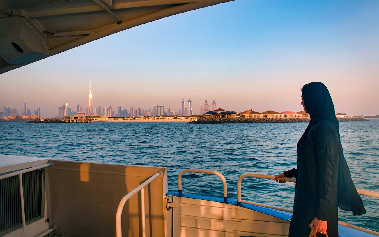 Woman on a boat with Dubai skyline and Burj Khalifa in the background.