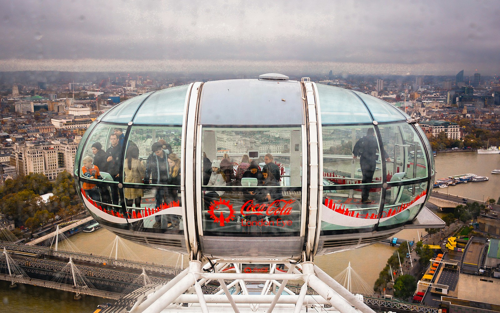 London Eye capsule with tourists overlooking the Thames River and cityscape.
