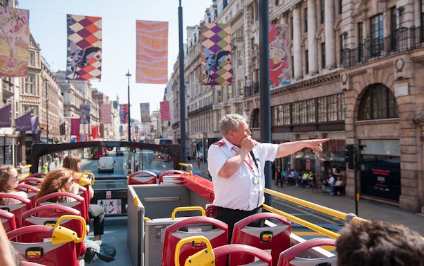 Open-top bus tour guide pointing on London street.