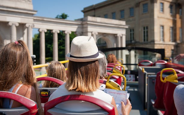 Open-top bus tour in London passing historical architecture.