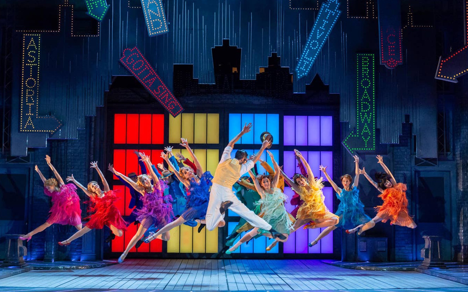 Performers dancing energetically on stage in "Singin' In The Rain" musical.