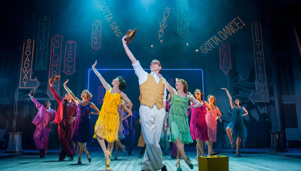 Performers dancing on stage in a vibrant "Singin' In The Rain" musical scene.