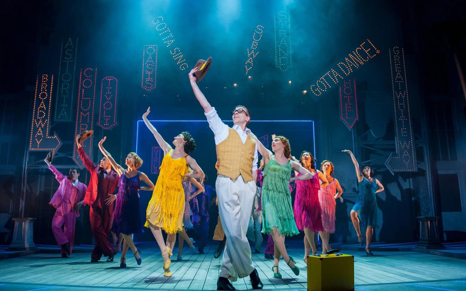 Performers dancing on stage in a vibrant "Singin' In The Rain" musical scene.