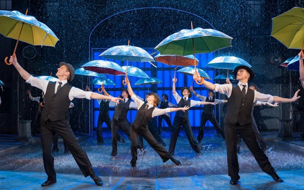 Performers dancing with umbrellas in a "Singin' In The Rain" stage show.
