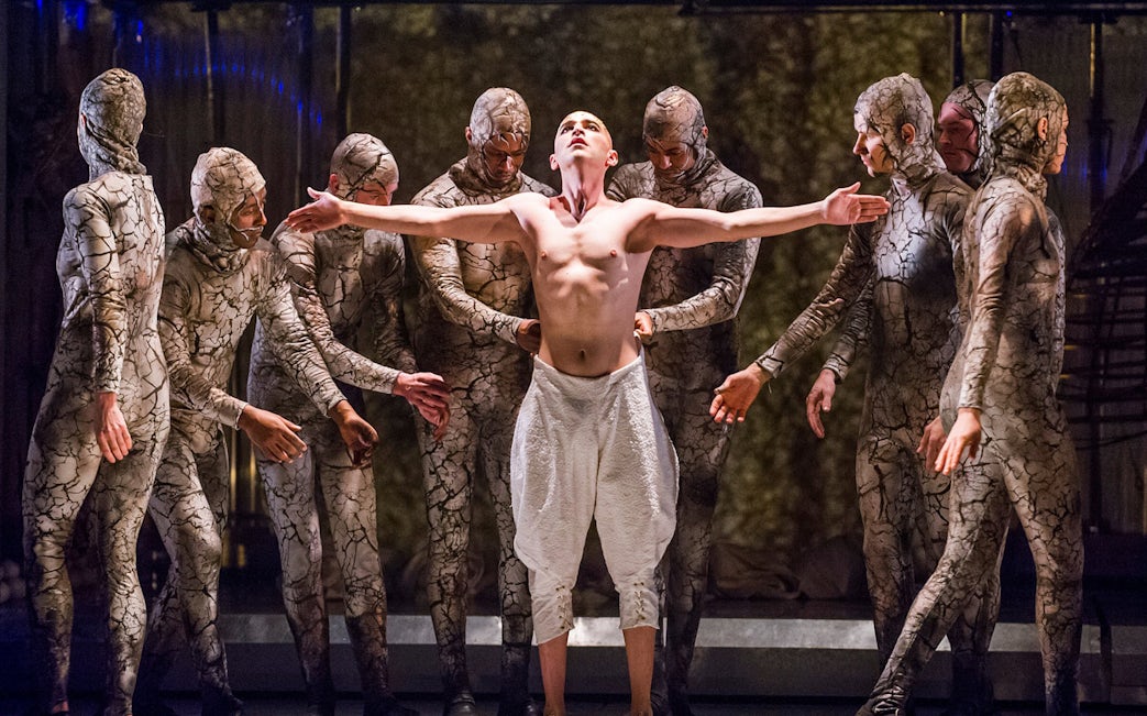 Performers in cracked earth costumes surround a central figure in the opera Akhnaten.