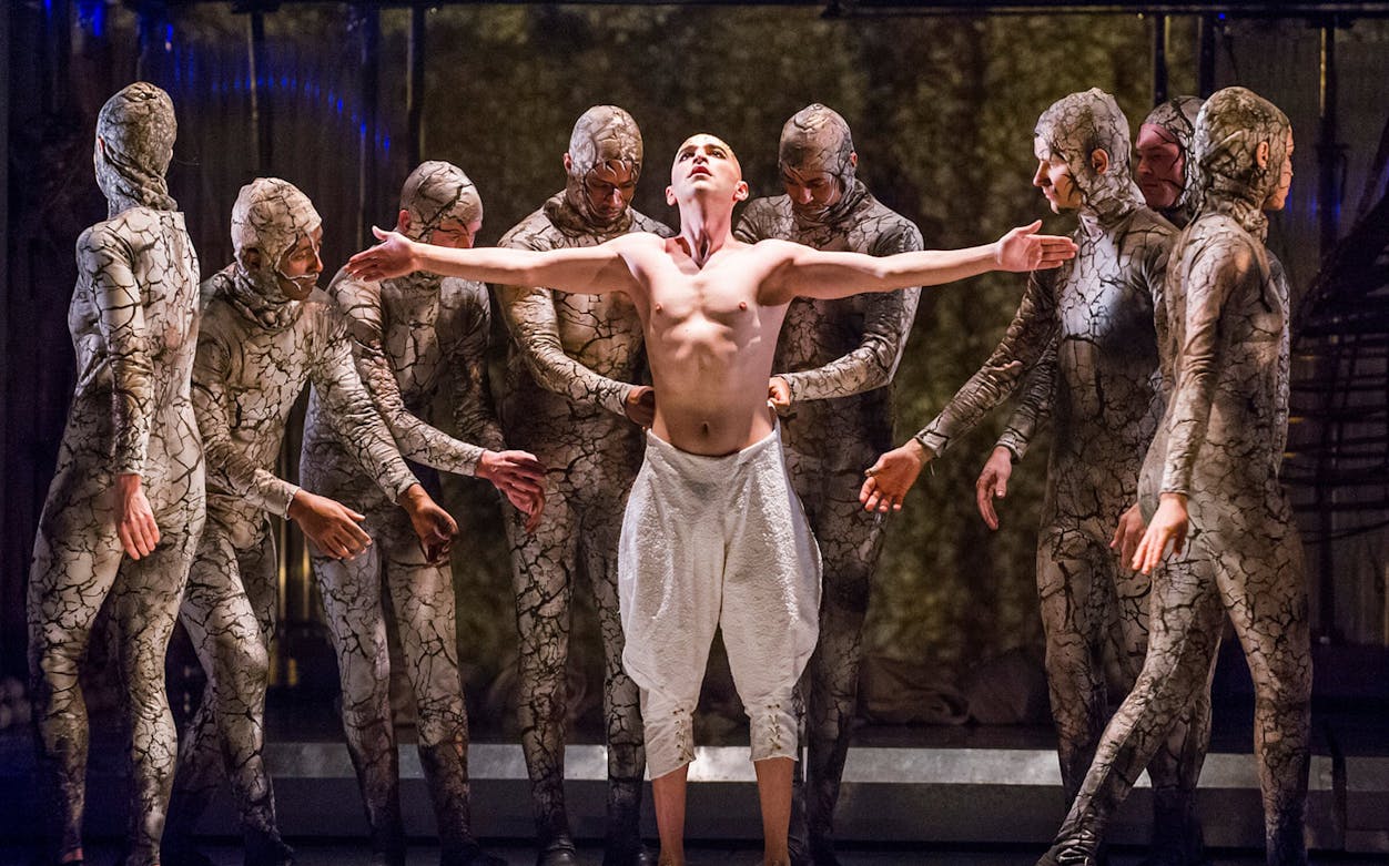 Performers in cracked earth costumes surround a central figure in the opera Akhnaten.