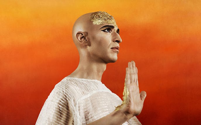 Opera performer in Akhnaten costume against a vibrant orange background.