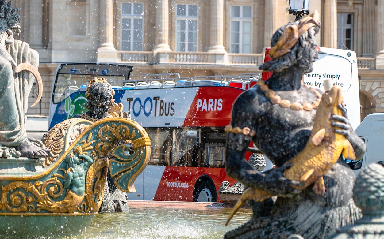 Paris hop-on-hop-off bus near ornate fountain statues.
