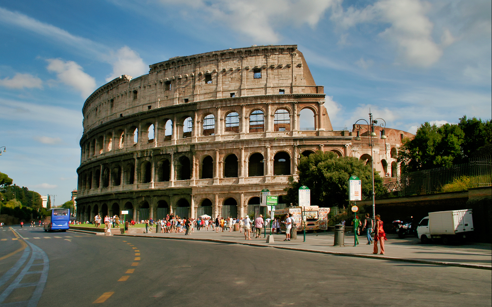 Colosseum in Rome with tourists and a blue hop-on-hop-off bus nearby.