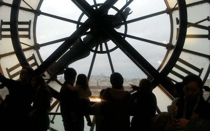 View of Paris through Orsay Museum clock with visitors inside.