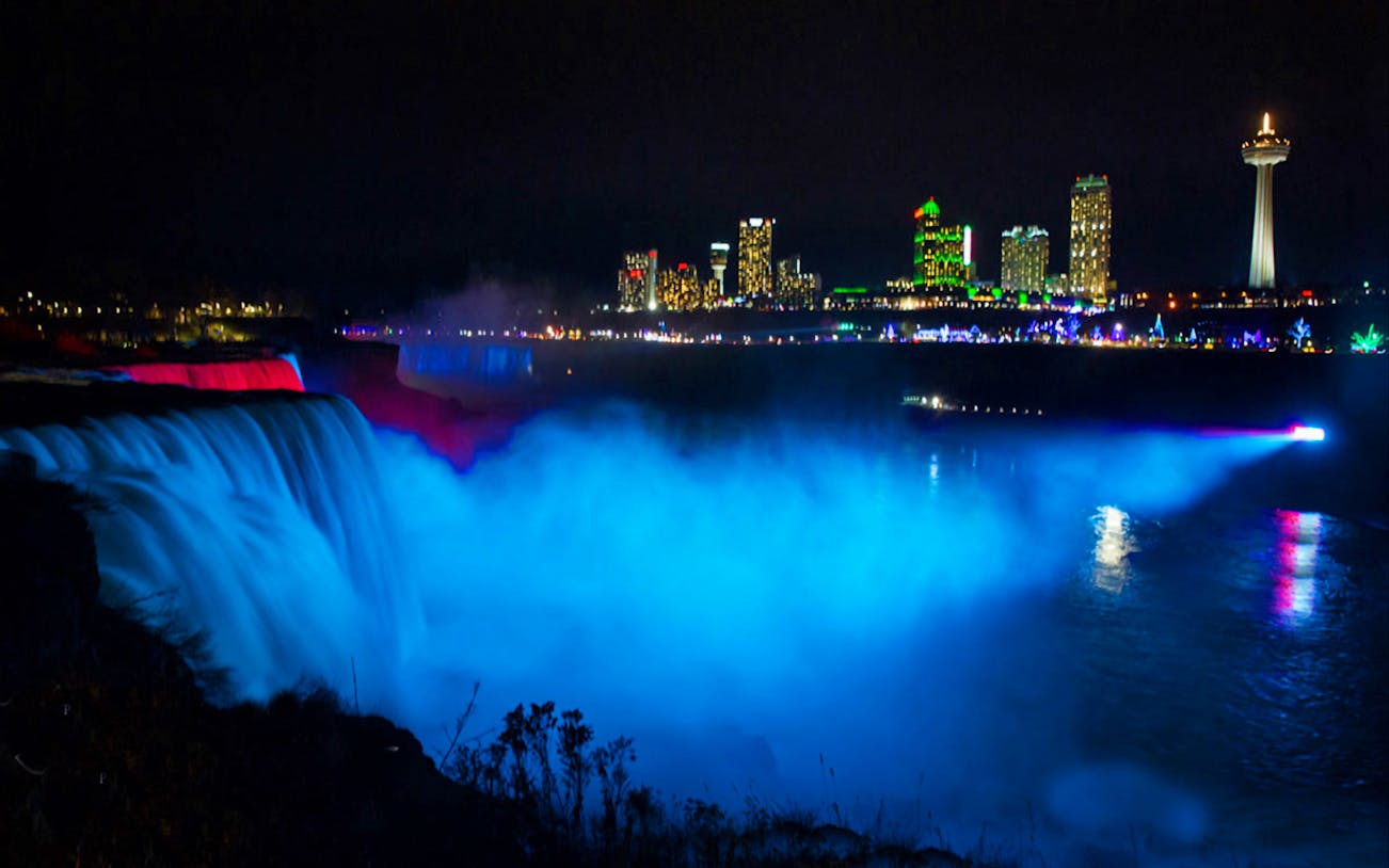 Niagara Falls illuminated at night with city skyline in the background.
