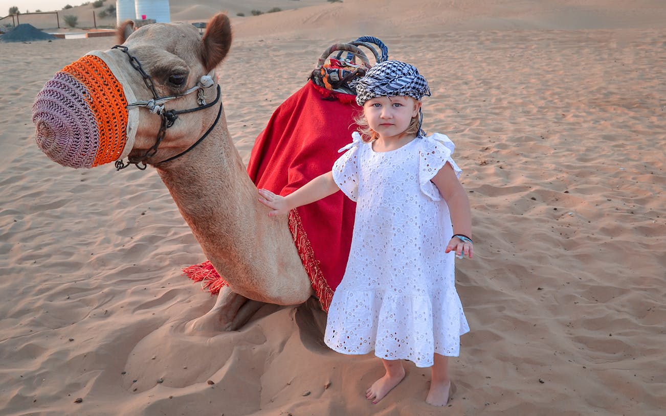 Child with camel in Dubai desert during shopping festival package.