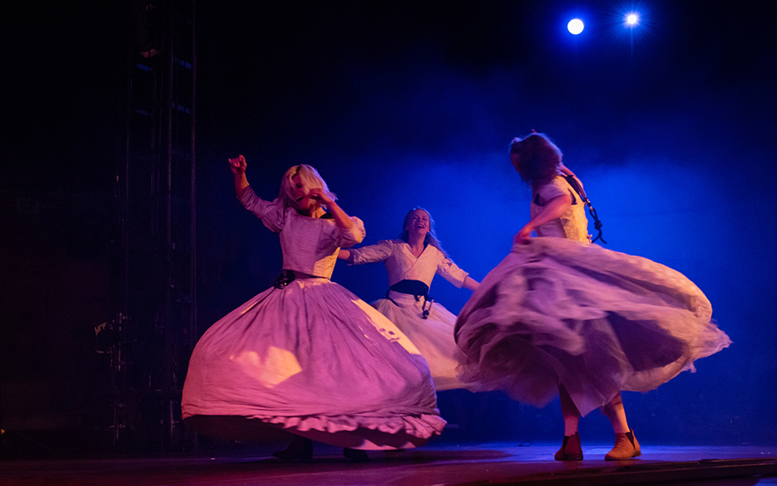 Dancers performing on stage in flowing dresses under blue lights.