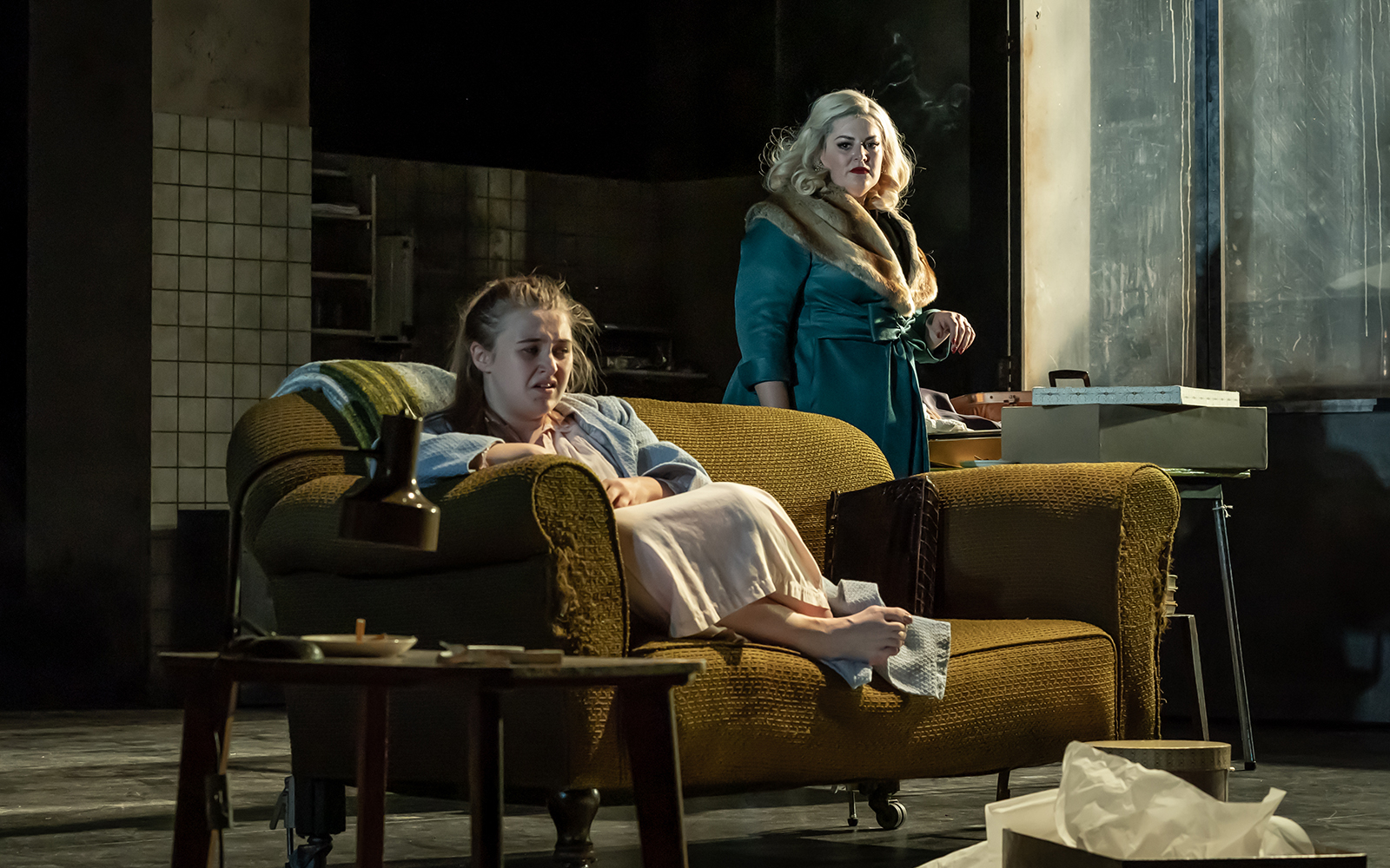 Two women in a dimly lit room, one seated on a sofa, the other standing, from "A Taste of Honey" play.