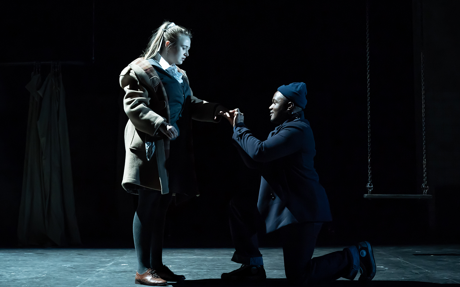 Two actors perform a scene from "A Taste of Honey" on stage, with one kneeling and holding the other's hand.