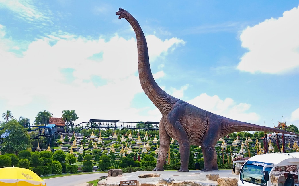 Brachiosaurus statue at Nong Nooch Tropical Garden, Thailand, with landscaped gardens in the background.