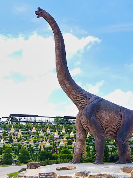 Brachiosaurus statue at Nong Nooch Tropical Garden, Thailand, with landscaped gardens in the background.