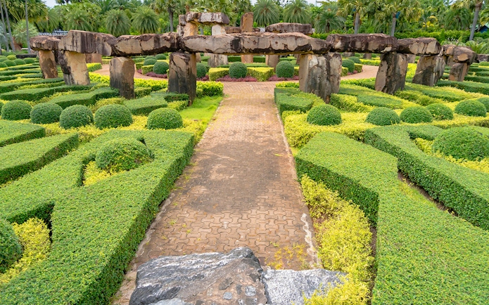 Pathway through manicured hedges and stone structures at Nong Nooch Tropical Garden, Thailand.