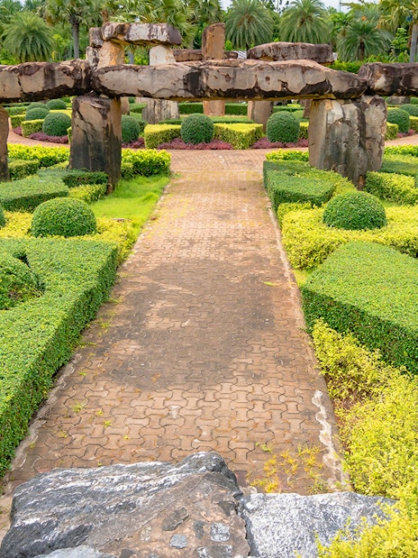 Pathway through manicured hedges and stone structures at Nong Nooch Tropical Garden, Thailand.