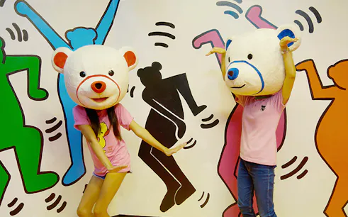 Visitors wearing bear costumes at Teddy Bear Museum Pattaya, posing in front of colorful mural.