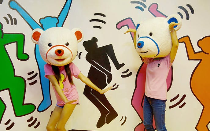 Visitors wearing bear costumes at Teddy Bear Museum Pattaya, posing in front of colorful mural.