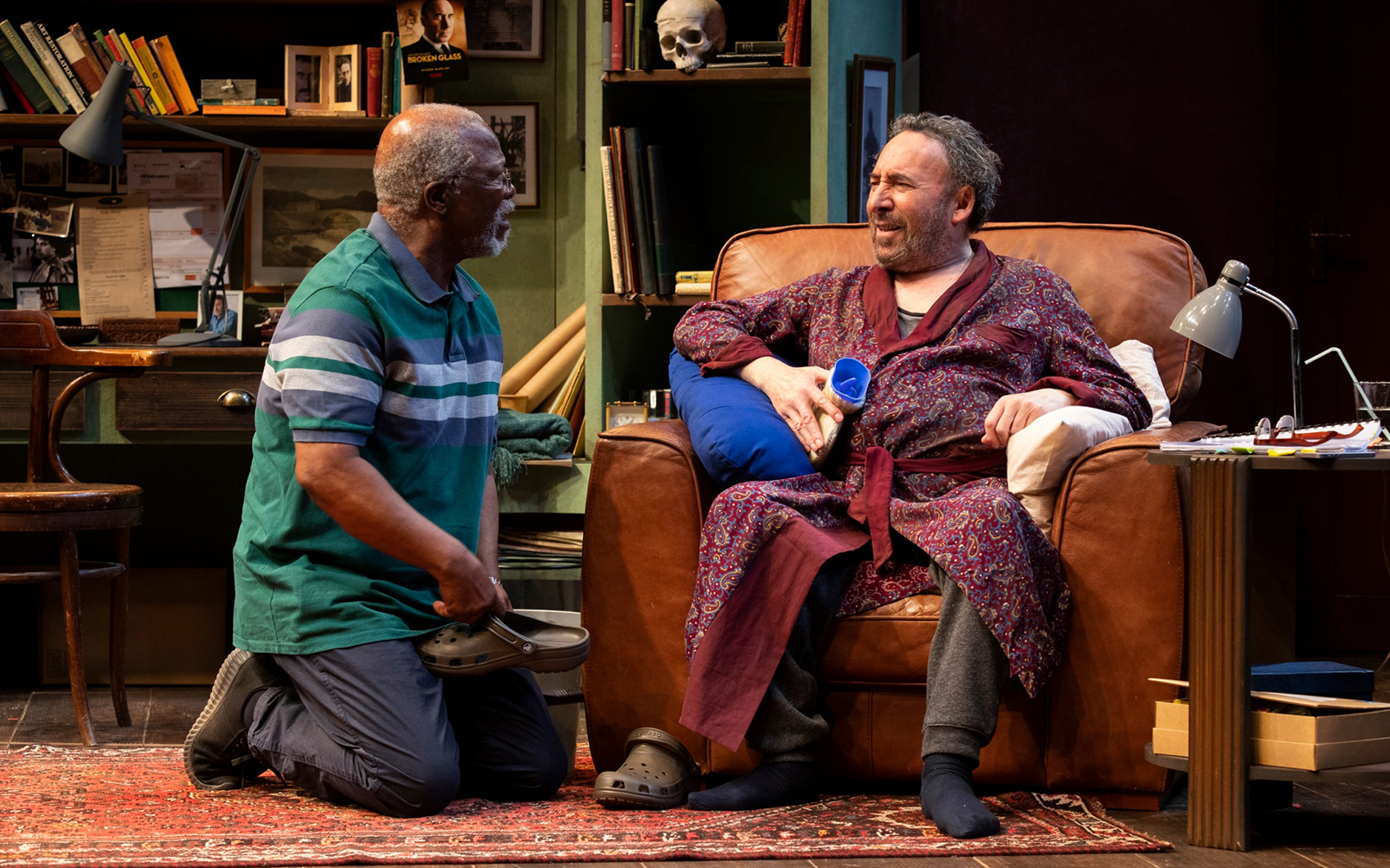 Two actors in a living room set, one seated in a chair, the other kneeling, from "Kunene and the King.