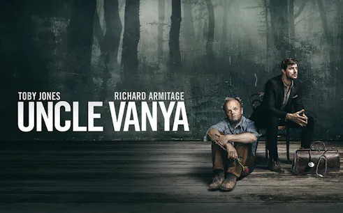 Uncle Vanya stage production with two men seated, one holding a rose, against a dark backdrop.