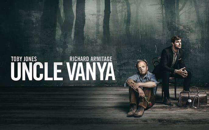 Uncle Vanya stage production with two men seated, one holding a rose, against a dark backdrop.