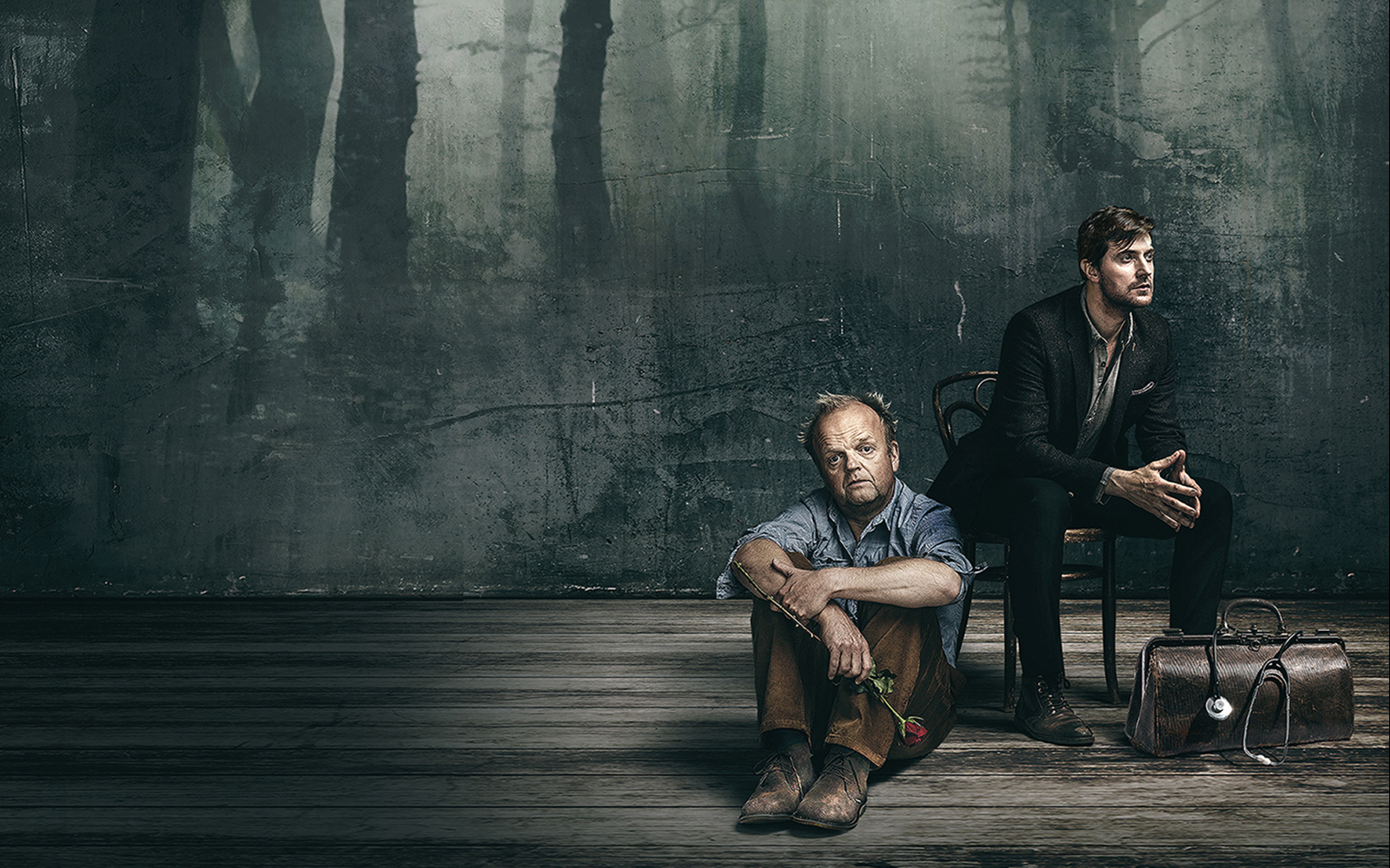 Two men in a dimly lit room, one seated on the floor holding a rose, related to Uncle Vanya.