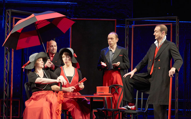 Performers in red and black costumes on stage during Showstopper! The Improvised Musical.