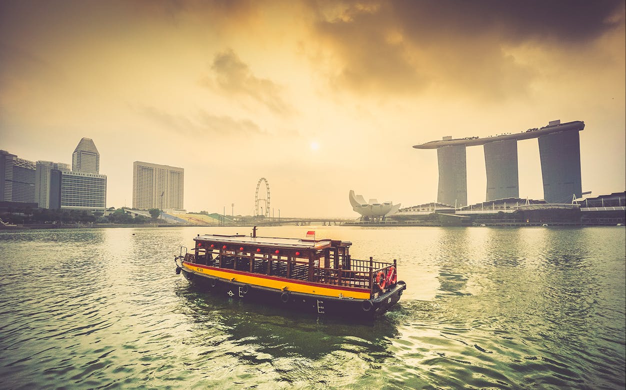 Singapore river cruise boat with Marina Bay Sands and skyline at sunset.