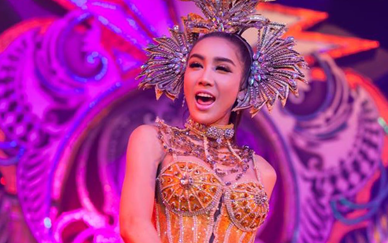 Performer in ornate costume at Aphrodite Cabaret Show, vibrant stage backdrop.