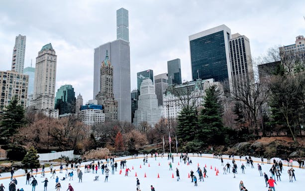 Ice skaters at Central Park with New York City skyline in the background.