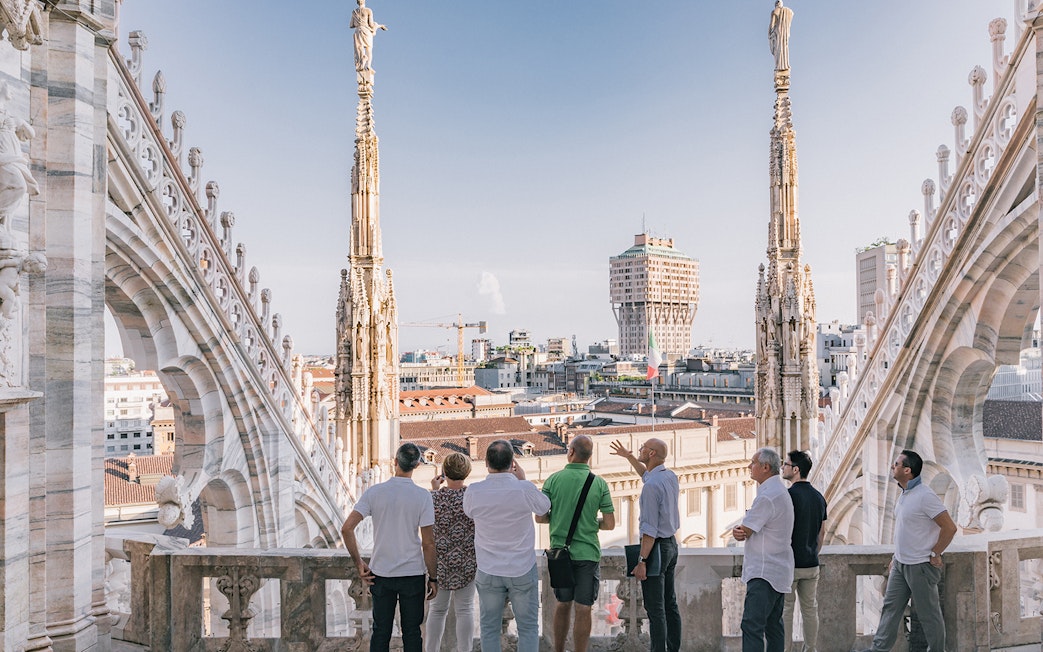 Visitors on Milan Duomo rooftop with city skyline in view.