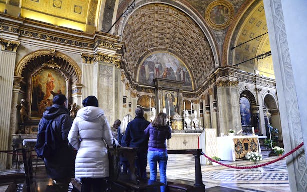 Visitors inside Milan's Duomo admiring ornate interior and religious artwork.