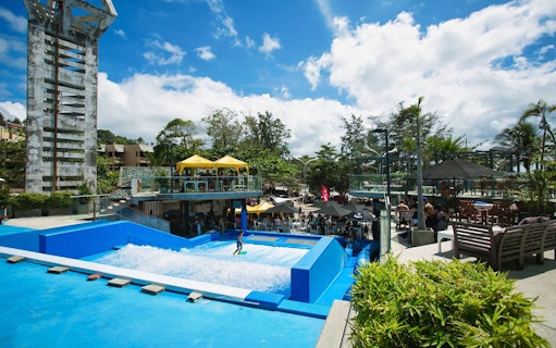 Surfer on artificial wave at Surf House Phuket Kata Beach, surrounded by spectators.