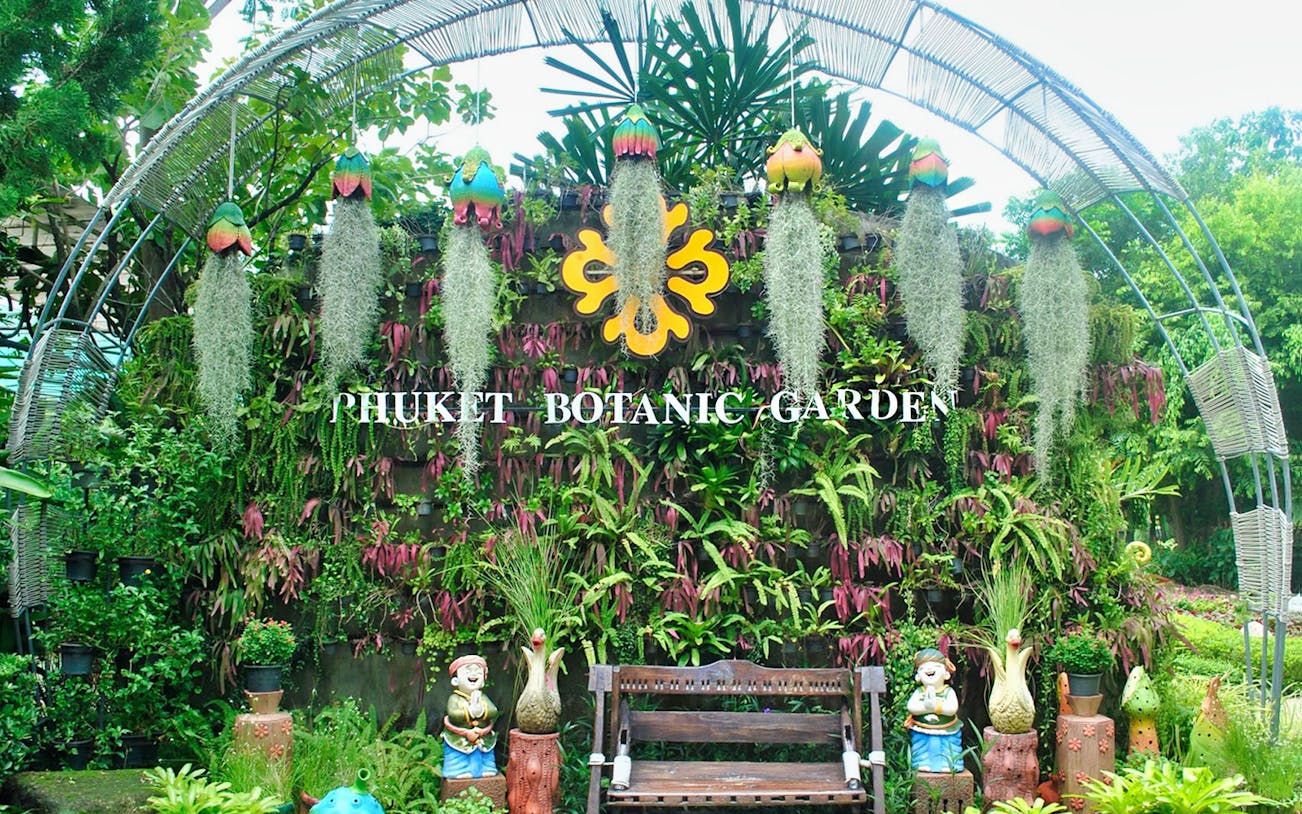 Phuket Botanic Garden entrance with lush greenery and decorative statues.